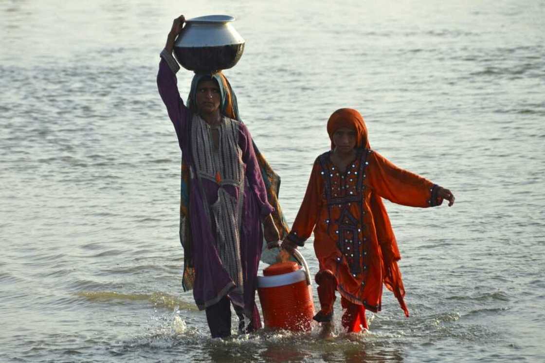 Girls wade through floodwater while carrying drinking water in Jaffarabad, Balochistan