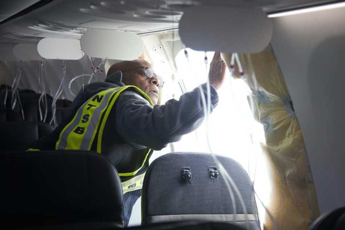 A man inspects a hole in the cabin of a Boeing airplane, the result of a fuselage panel blowing off mid-flight