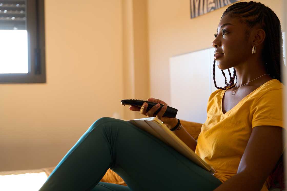 A young woman watching TV and holding a remote control