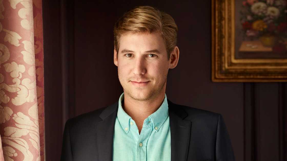 Austen Kroll poses standing for a portrait in a black suit and a green shirt. Austen Kroll poses standing for a portrait in a black suit and a green shirt.