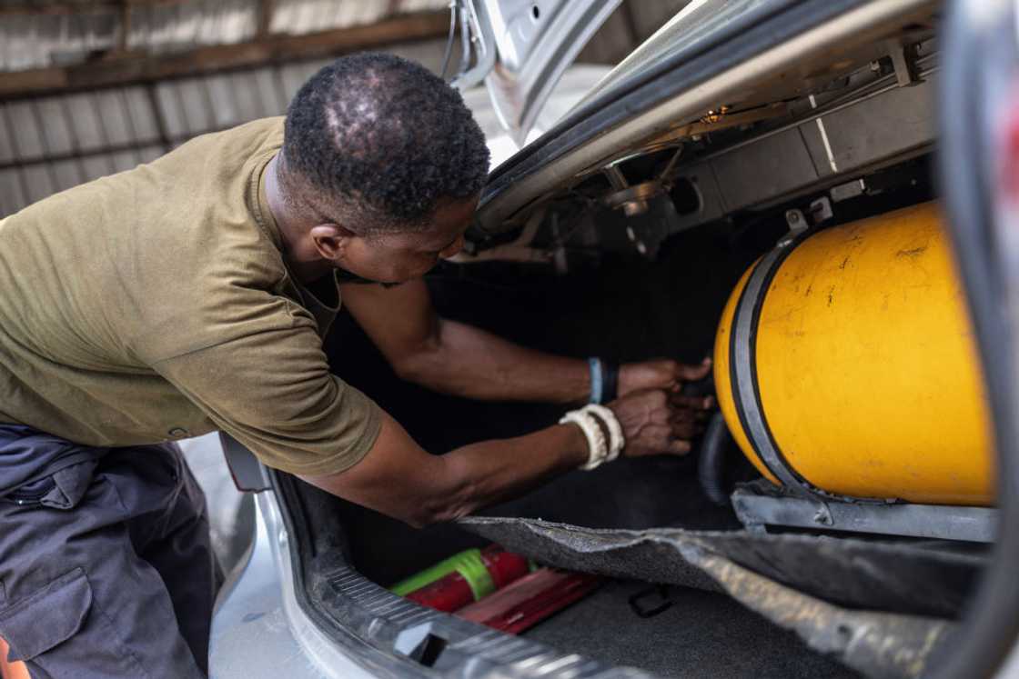 Mechanical engineer Tajudeen Esan leaning into a car boot as he fits a yellow gas cylinder for a CNG conversion at a workshop in Lagos, 2024