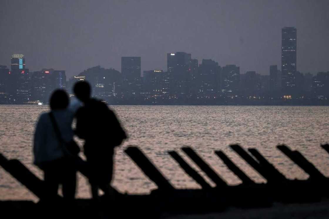 Visitors stand on a beach with anti-landing barricades with the Chinese city of Xiamen seen in the background