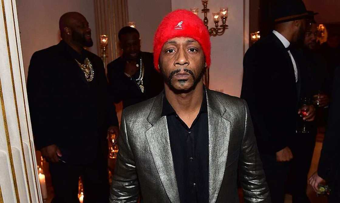 Katt Williams in a dark gray coat, black shirt and red Marvin