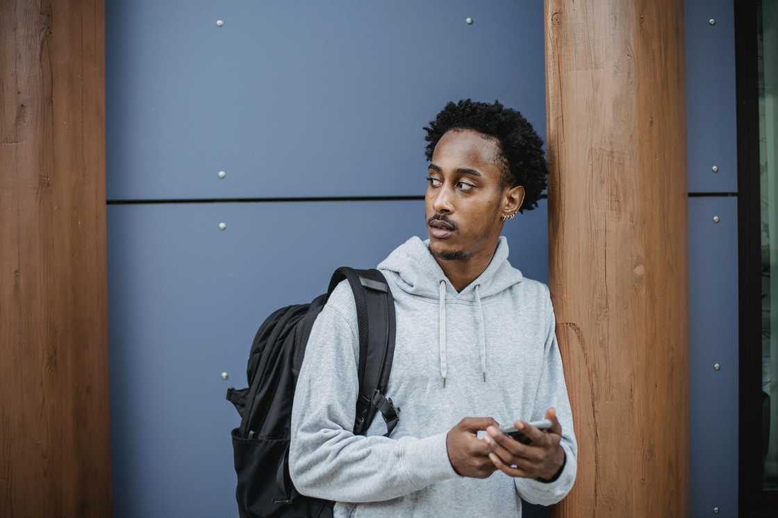 A serious young man in a grey hoodie is scrolling on his smartphone