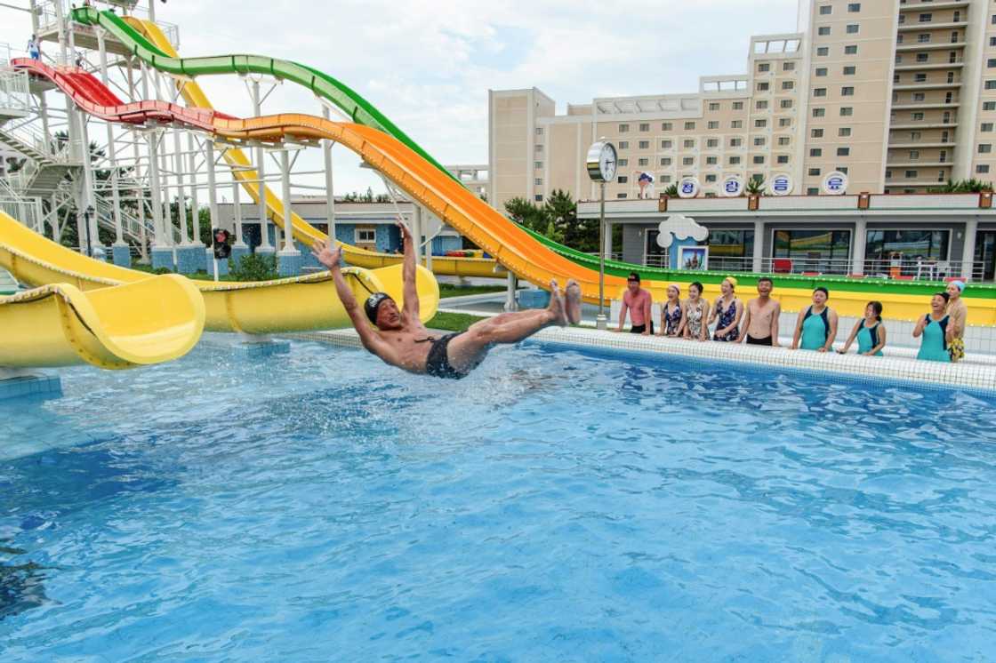 Domestic tourists watch as a man uses a slide into a swimming pool at the Myongsasimni Water Park in North Korea