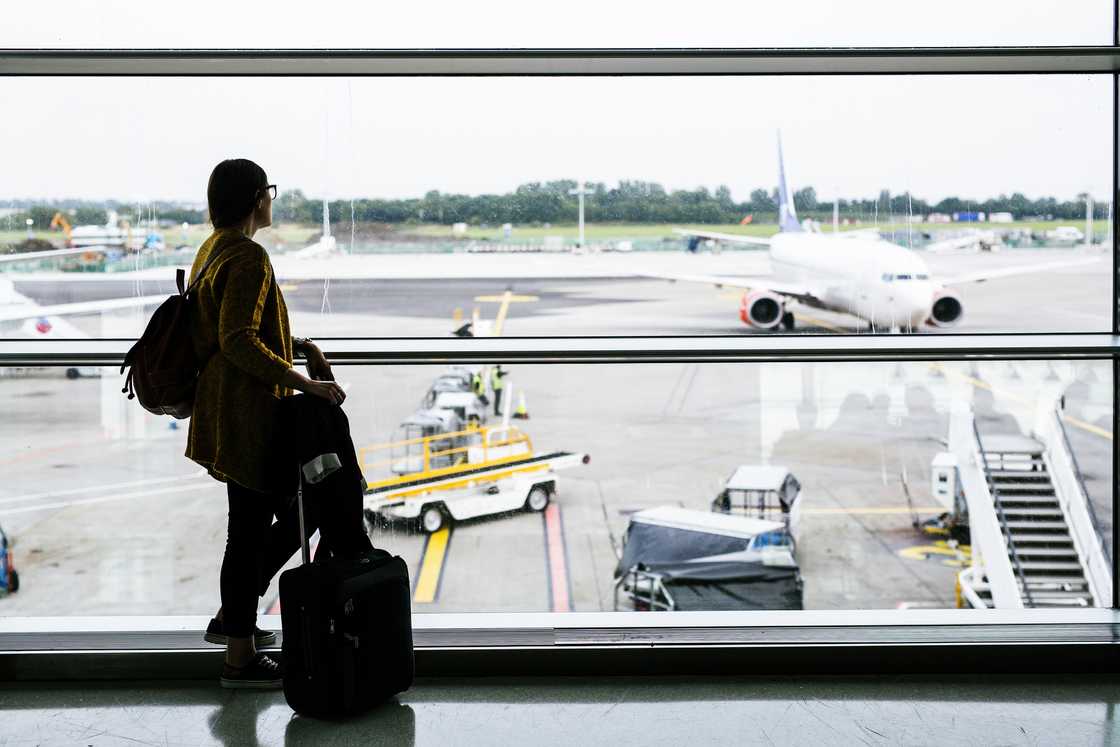 A woman watches through glass as her plane departs without her. A woman watches through glass as her plane departs without her.