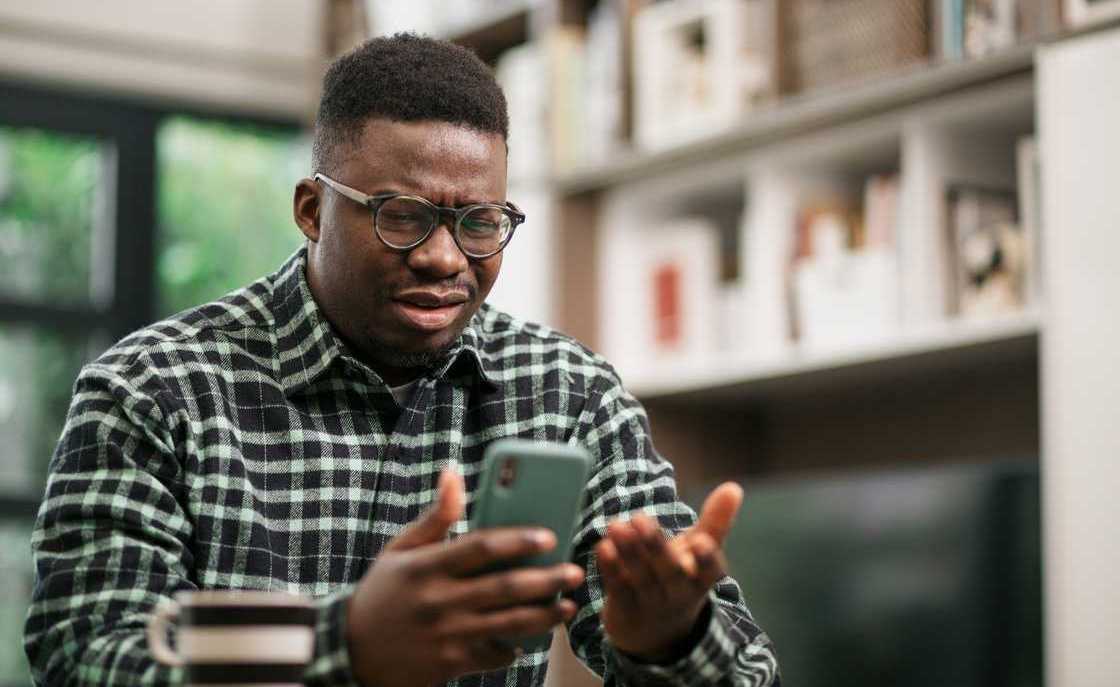 An annoyed young man gestures while checking his phone
