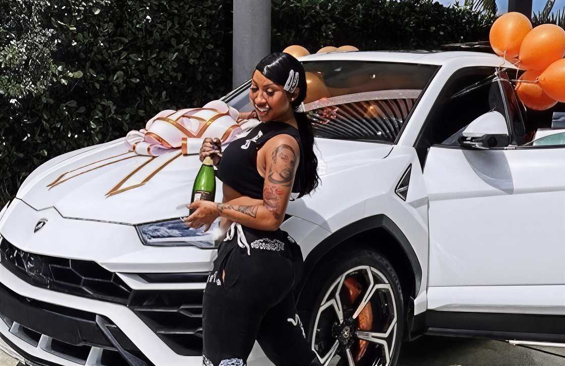 Moneybagg Yo poses with a wine bottle in front of her a white Lamborghini Urus for her birthday