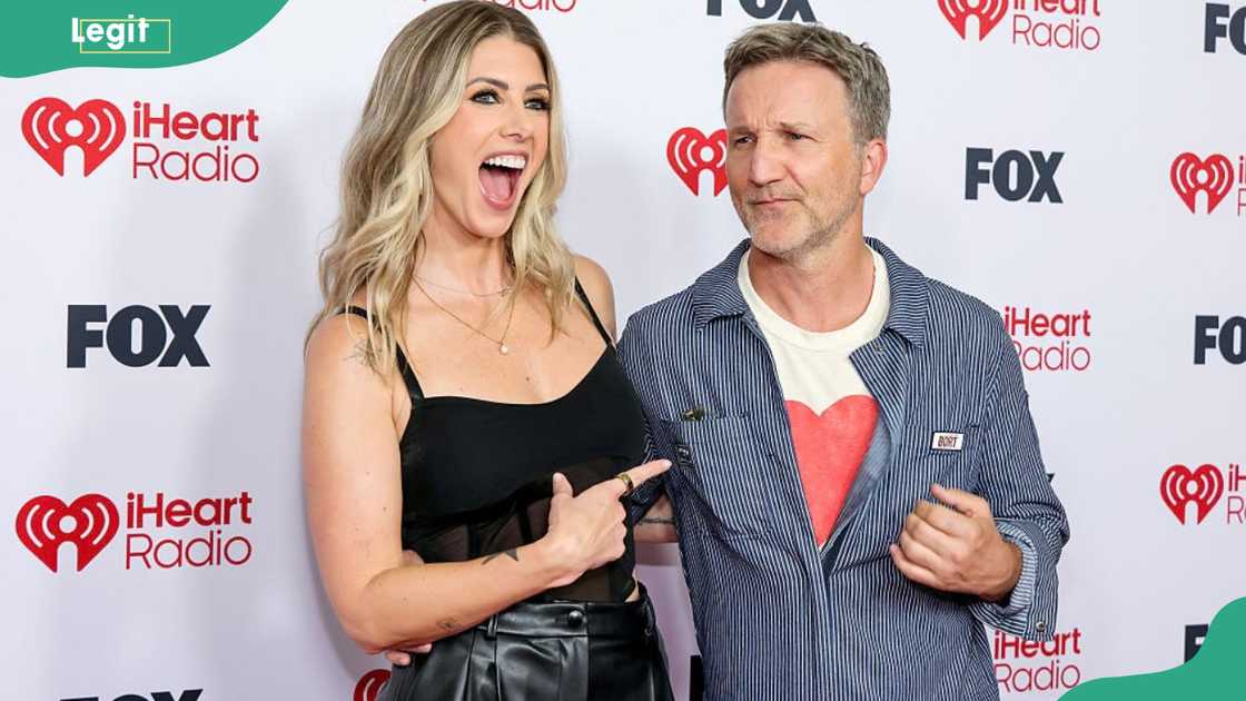 A laughing woman in a black top points at a man in a striped jacket making a face.