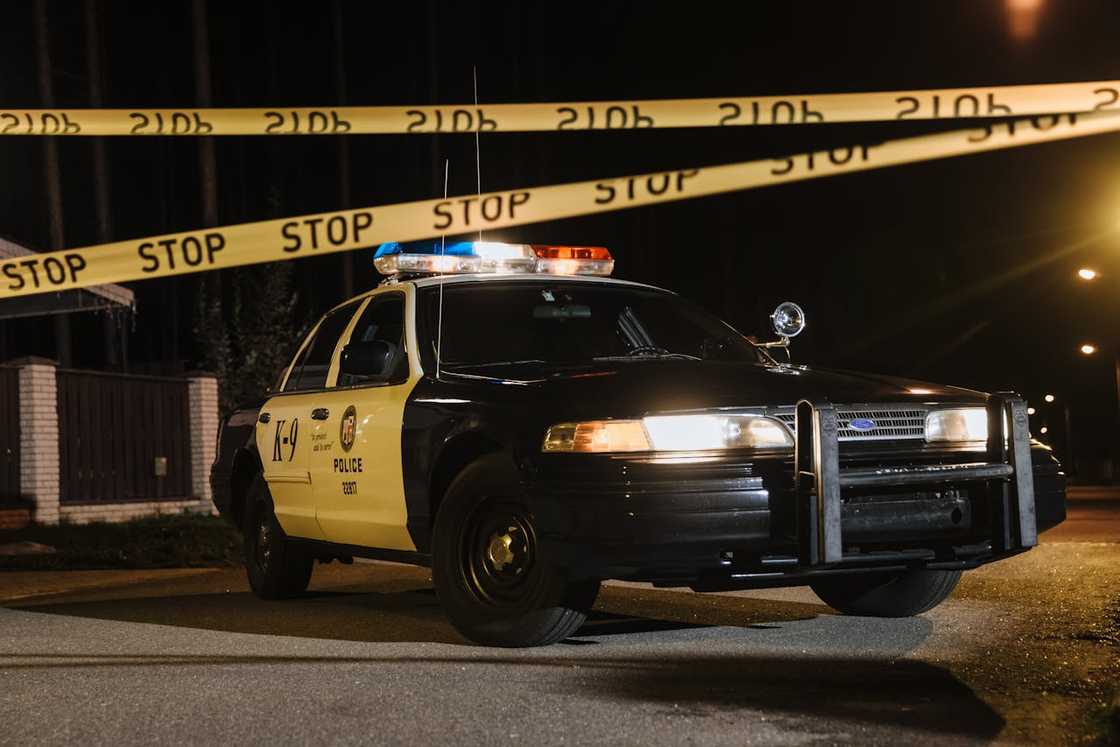A police car parked at night behind yellow “STOP” crime-scene tape.