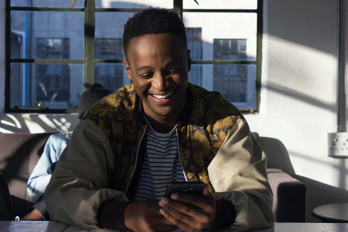 A happy young man in a striped tee and jacket is using a smartphone