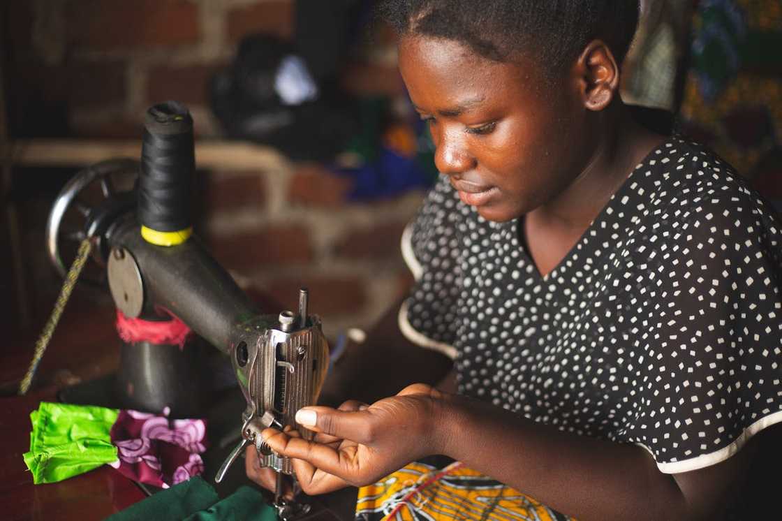 A young woman carefully threading a needle on a sewing machine in a small workshop.