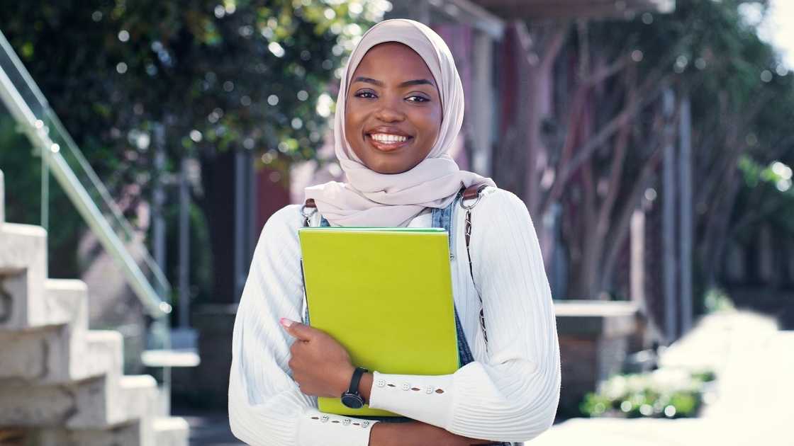 A female Muslim student poses holding books. A female Muslim student poses holding books.
