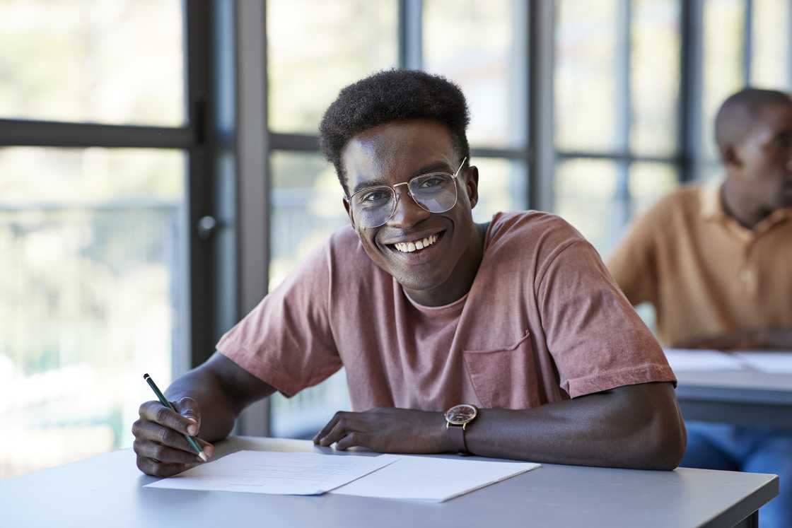 A young male student sitting with exam papers in a community college classroom.