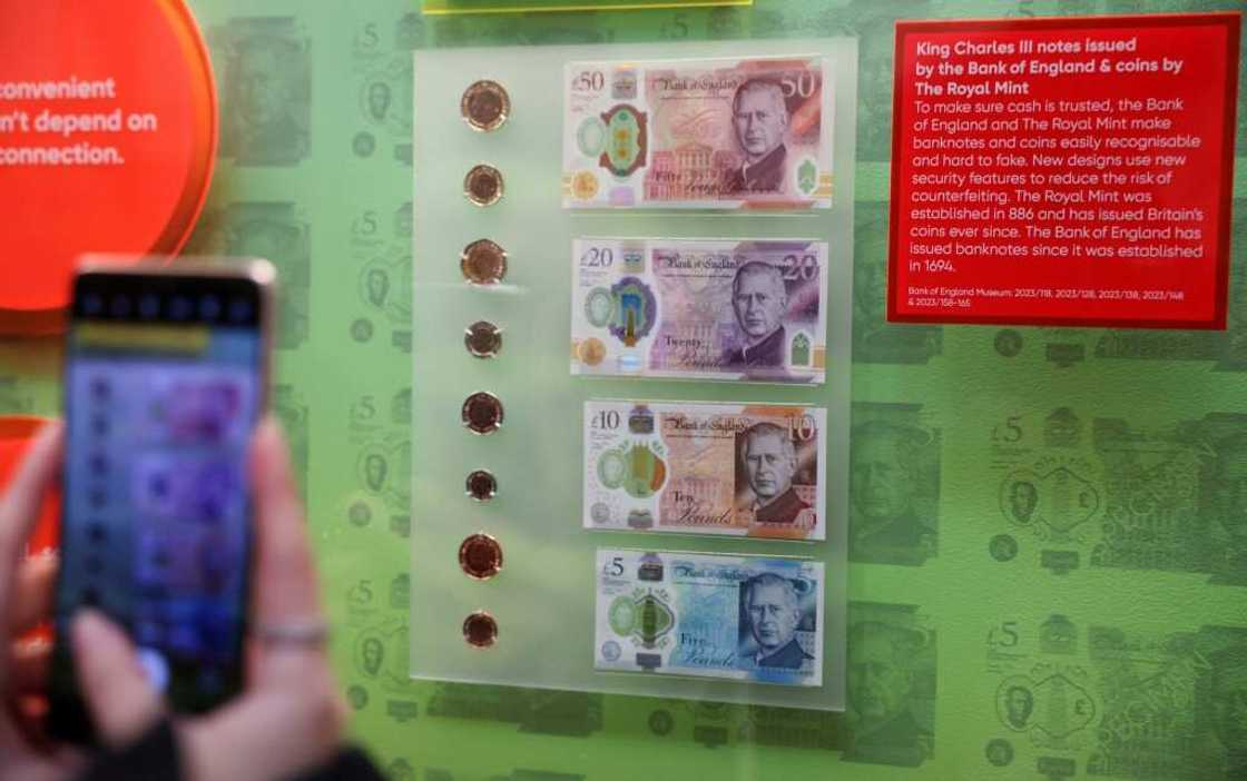 Members of the media photograph banknotes and coins that feature an image of Britain's King Charles III, during a photocall for 'The Future of Money' exhibition, at the Bank of England Museum in London on February 27, 2024 Members of the media photograph banknotes and coins that feature an image of Britain's King Charles III, during a photocall for 'The Future of Money' exhibition, at the Bank of England Museum in London on February 27, 2024