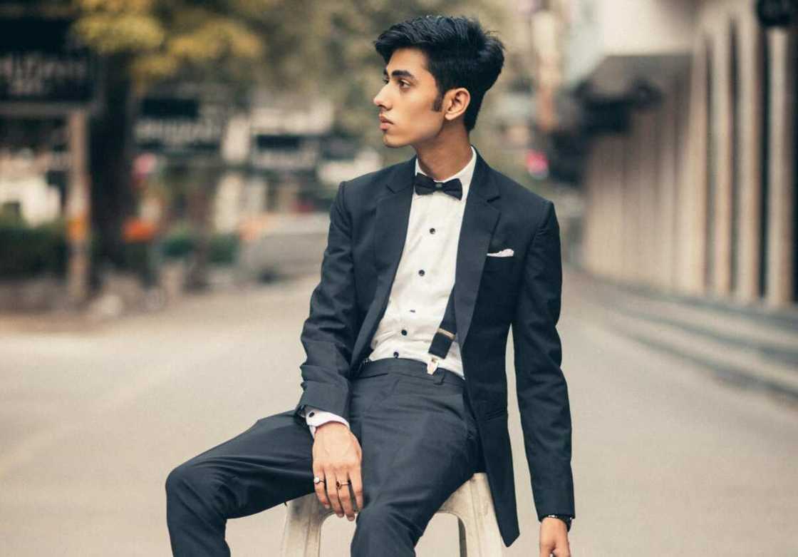 A man in a black tuxedo sitting on a white plastic chair