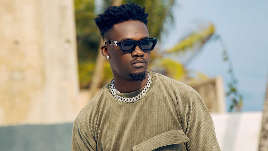Jason Jae from BBNaija poses outdoors in a green outfit and jewellery.