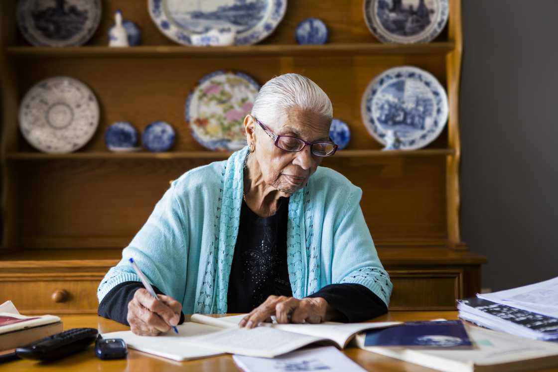 An elderly person studying at a table. An elderly person studying at a table.