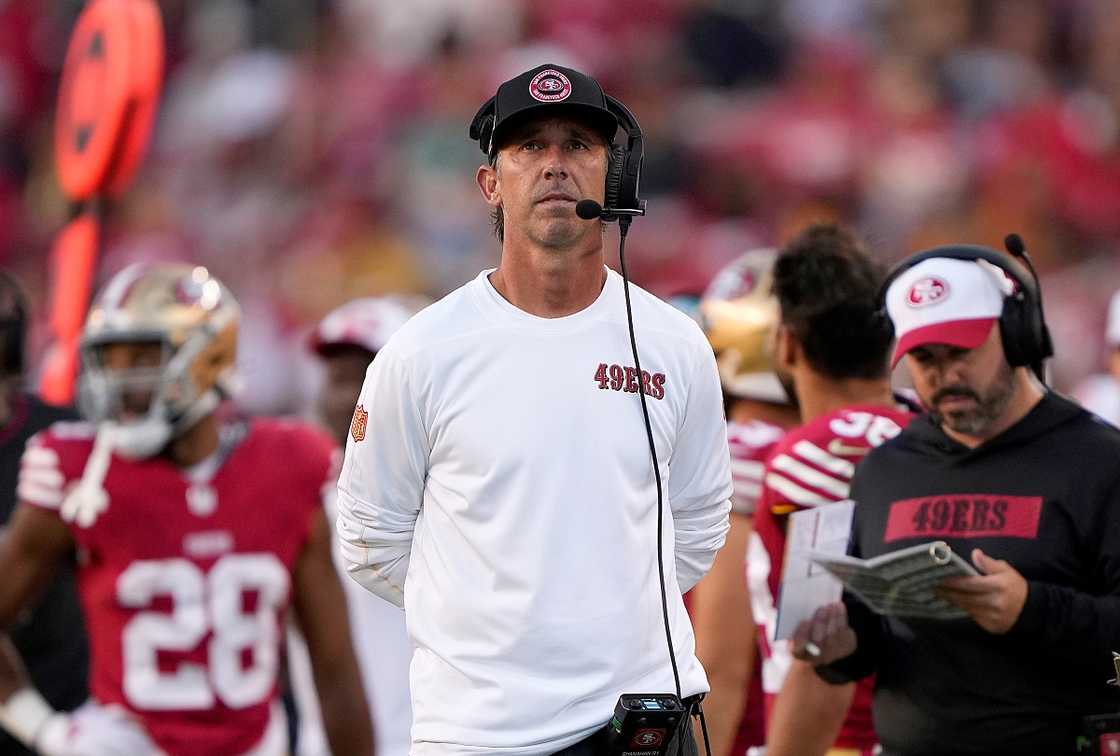 Kyle Shanahan (C) looks on during a football game in a white outfit.