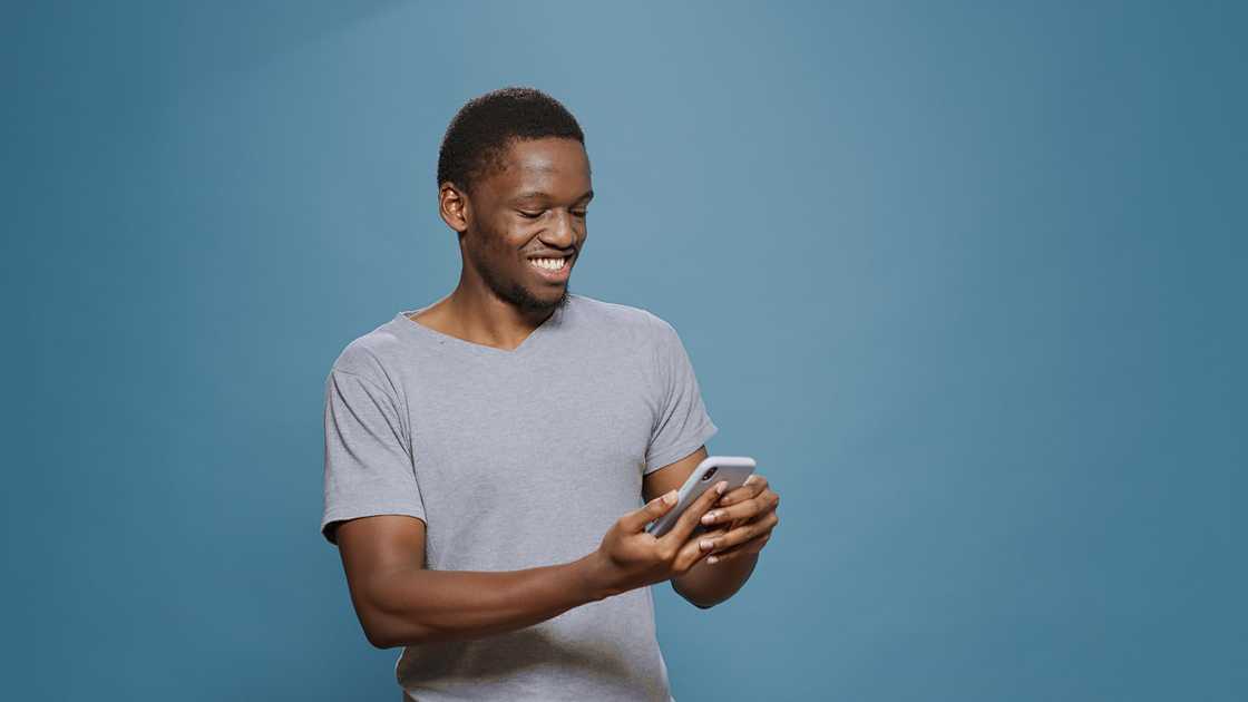 A young man smiling while using his phone