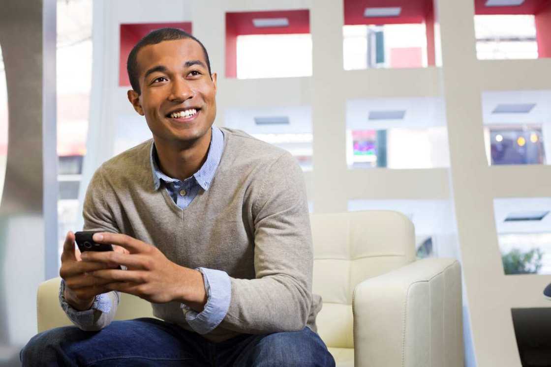A smiling man sitting a couch and holding a phone A smiling man sitting a couch and holding a phone