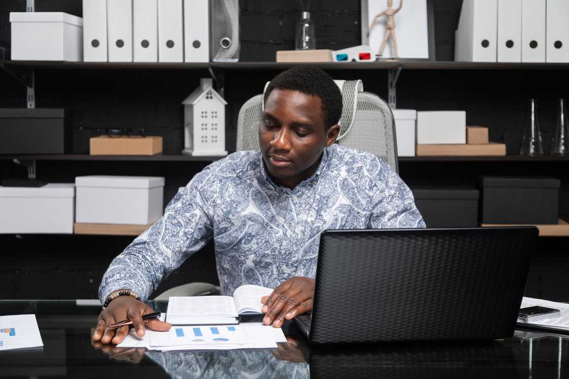 A male financier working on a project using a notebook and a laptop. A male financier working on a project using a notebook and a laptop.