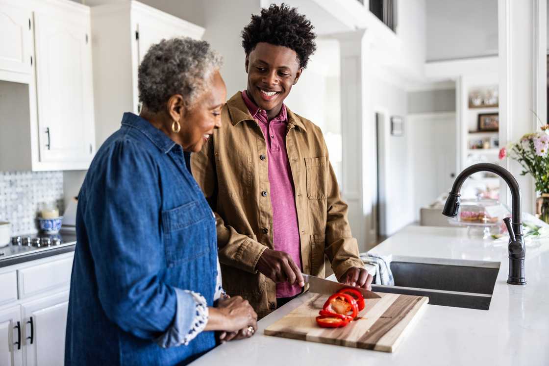 An elderly woman helps his teenage grandson in the kitchen.