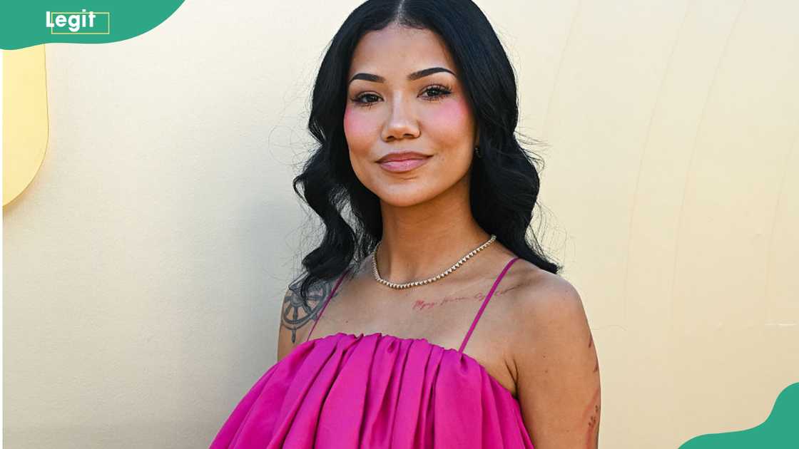 Jhené Aiko poses against a cream backdrop wearing a hot pink strappy dress and pearl necklace. Jhené Aiko poses against a cream backdrop wearing a hot pink strappy dress and pearl necklace.