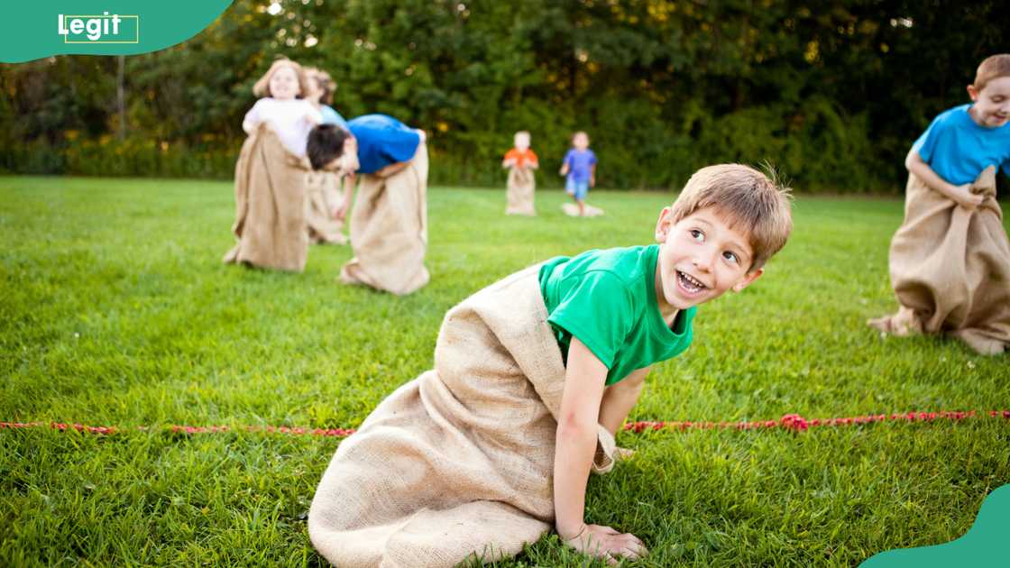 A group of happy kids laughing and enjoying a potato sack race outside.