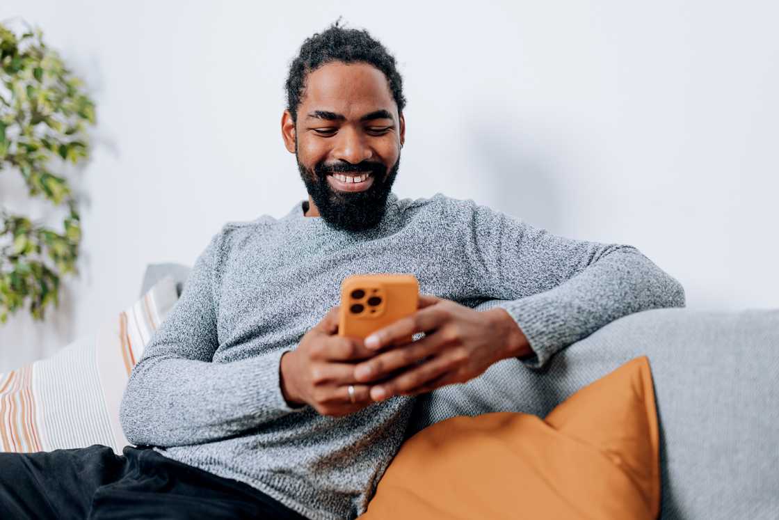 A young African American man is looking at his phone with a smile on his face.