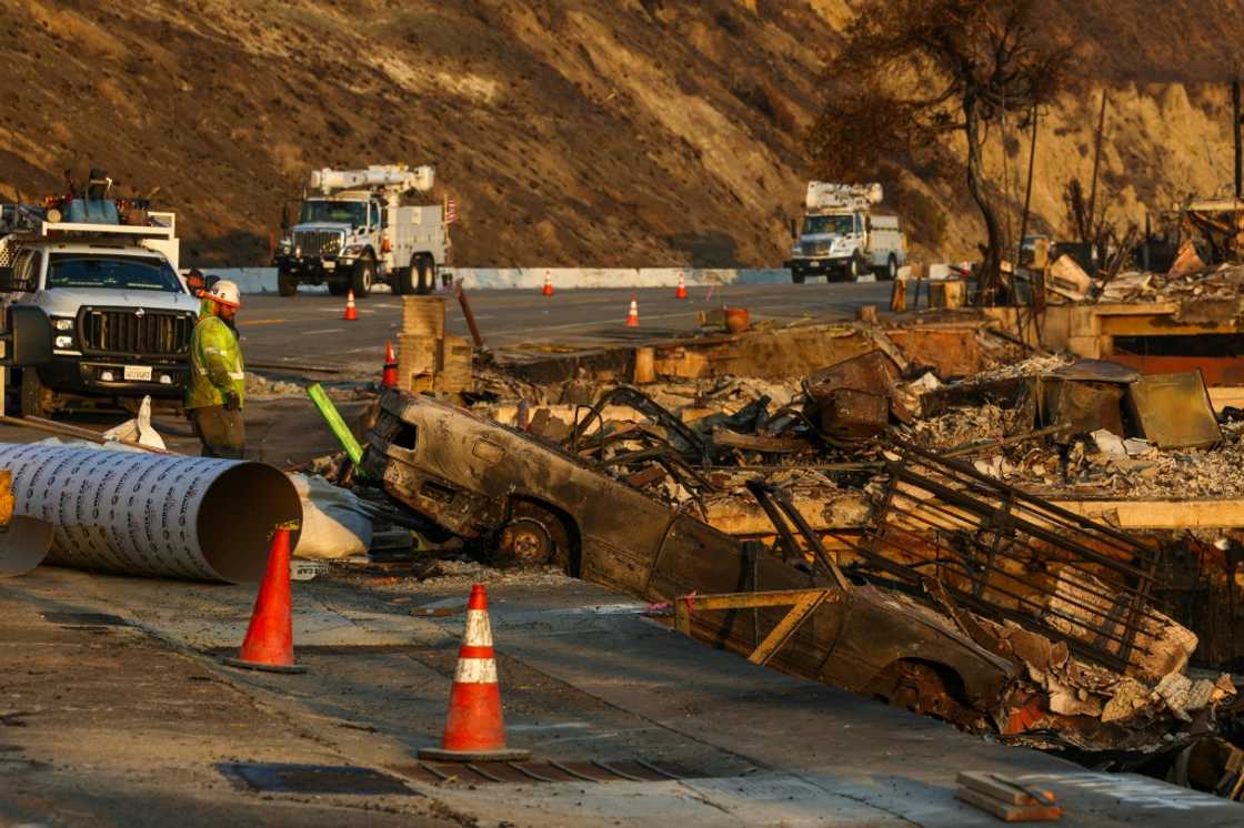 Edison employees look at burned remains of a car as they work to restore electricity along the Pacific Coast Highway in Malibu, California on January 19, 2025 Edison employees look at burned remains of a car as they work to restore electricity along the Pacific Coast Highway in Malibu, California on January 19, 2025