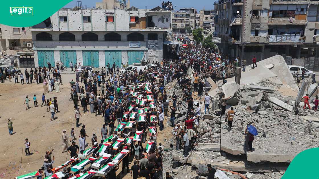 Palestinian flags drape rows of bodies while relatives mourn and carry them for burial.