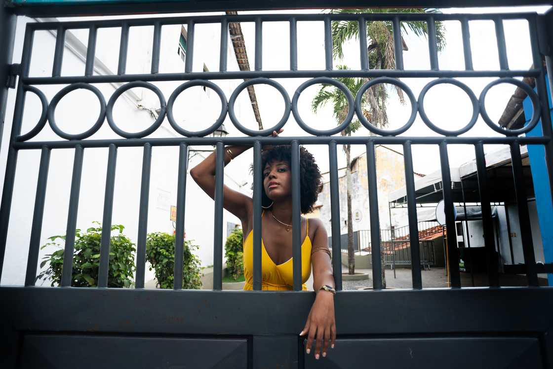A mother wearing yellow clothes with afro hair next to a gate A mother wearing yellow clothes with afro hair next to a gate