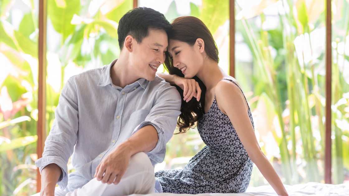 A young couple is pictured together on a bed against a lush green background.