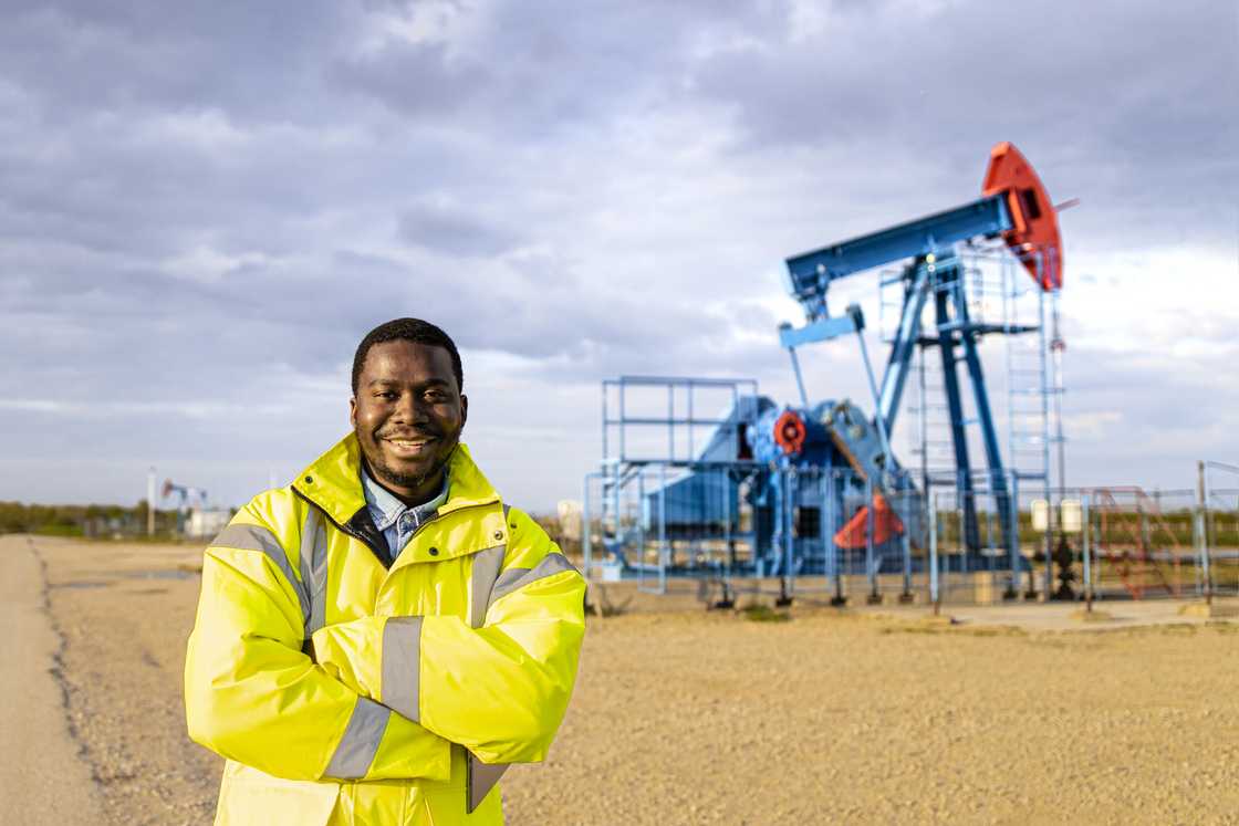 An oil field worker standing in front of oil rigs drilling crude oil. An oil field worker standing in front of oil rigs drilling crude oil.