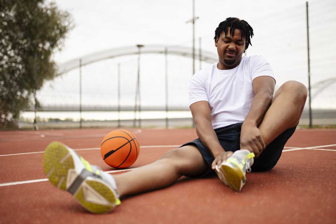 Basketball player holding his leg in pain on the court Basketball player holding his leg in pain on the court