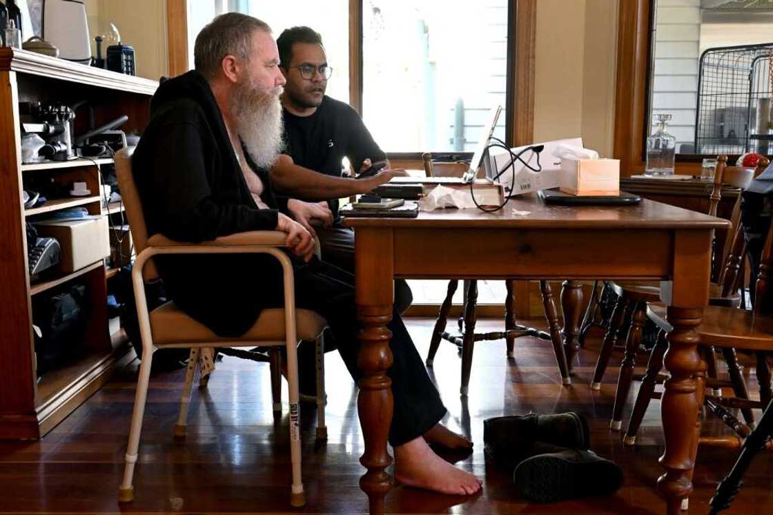 Rodney Gorham, who has a  Synchron brain implant, works on a computer at his home in Melbourne with clinical field engineer Zafar Faraz