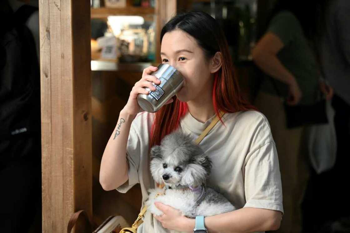 Pet groomer Lucine Mo drinks coffee out of a thermal mug with a QR code at a coffee shop in Hong Kong Pet groomer Lucine Mo drinks coffee out of a thermal mug with a QR code at a coffee shop in Hong Kong