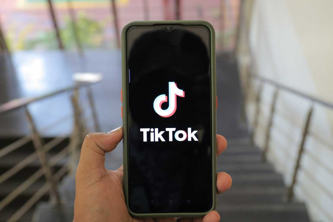A person holding a cellphone with a TikTok logo A person holding a cellphone with a TikTok logo