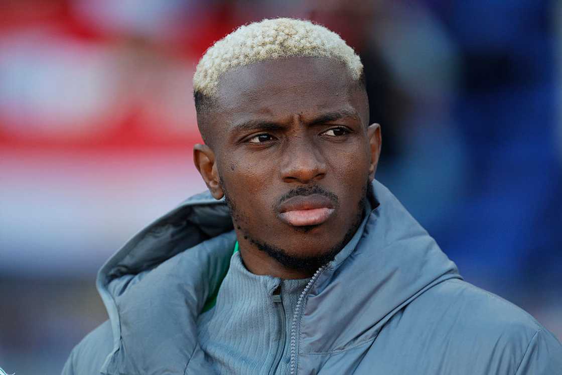 Victor Osimhen in a grey Nigeria team jacket with bleached blond hair, looking ahead