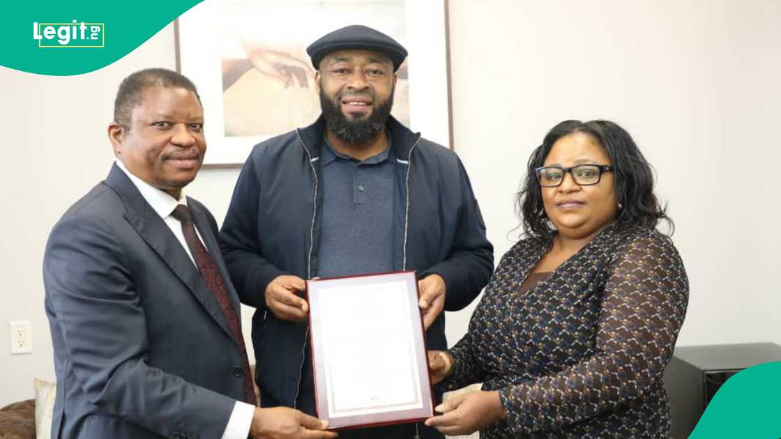 Governor stands in the middle of a man and woman, holding agreement documents Governor stands in the middle of a man and woman, holding agreement documents