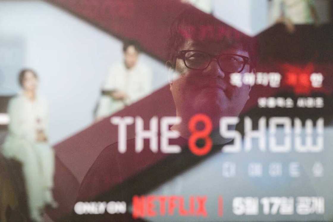 Bae Jin-soo, who created the Naver webtoons "Money Game" and "Pie Game" which inspired Netflix's "The 8 Show", poses in front of a framed poster for the show Bae Jin-soo, who created the Naver webtoons "Money Game" and "Pie Game" which inspired Netflix's "The 8 Show", poses in front of a framed poster for the show