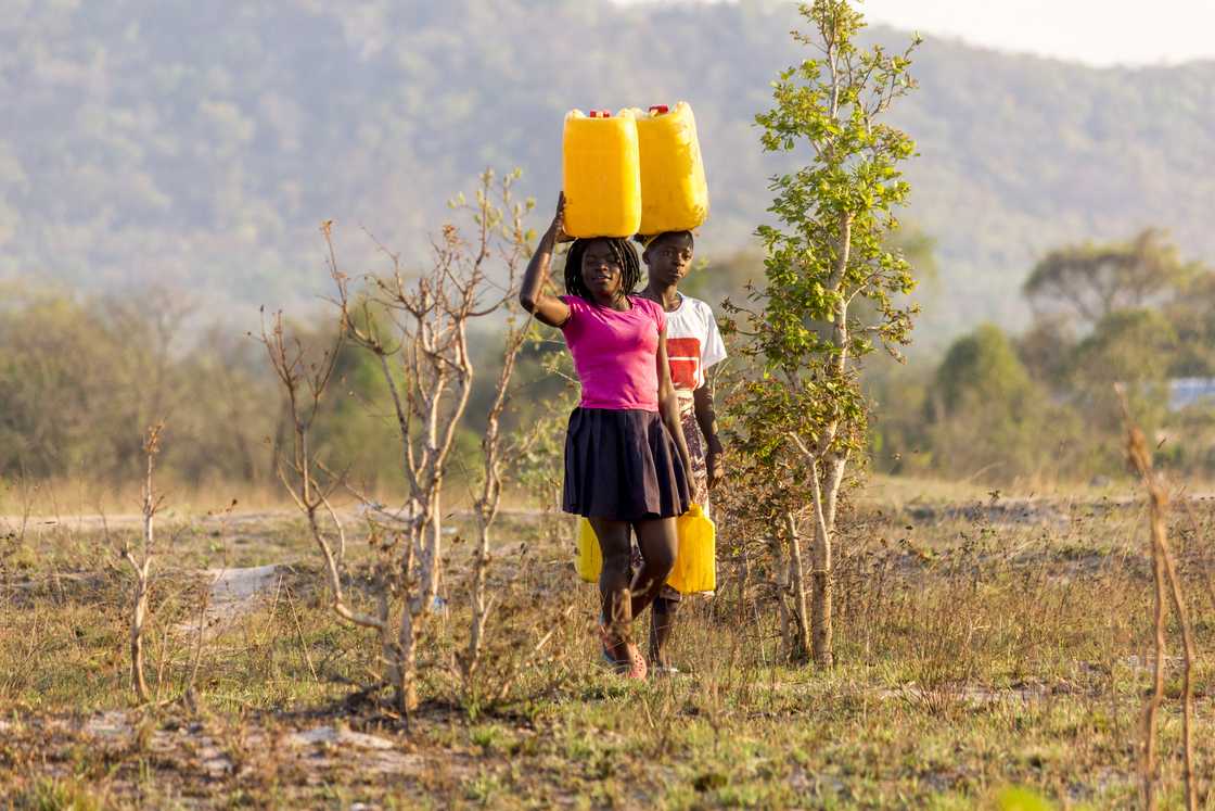 Two ladies carrying jerricans of water on their heads