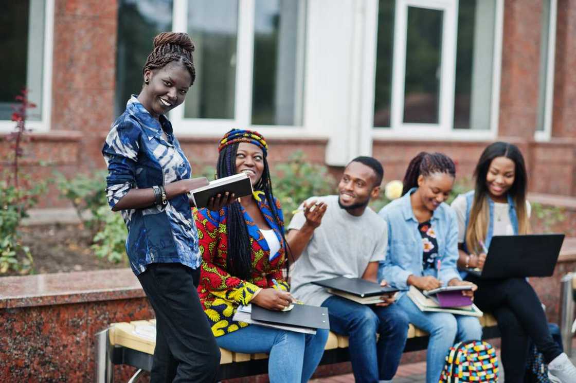 Group of five college students spending time together on campus at university yard.