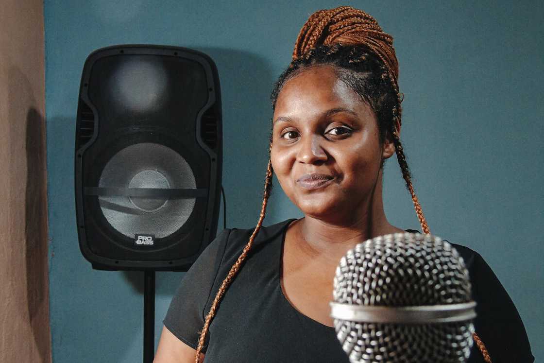 A woman standing in front of a microphone in a small recording studio.