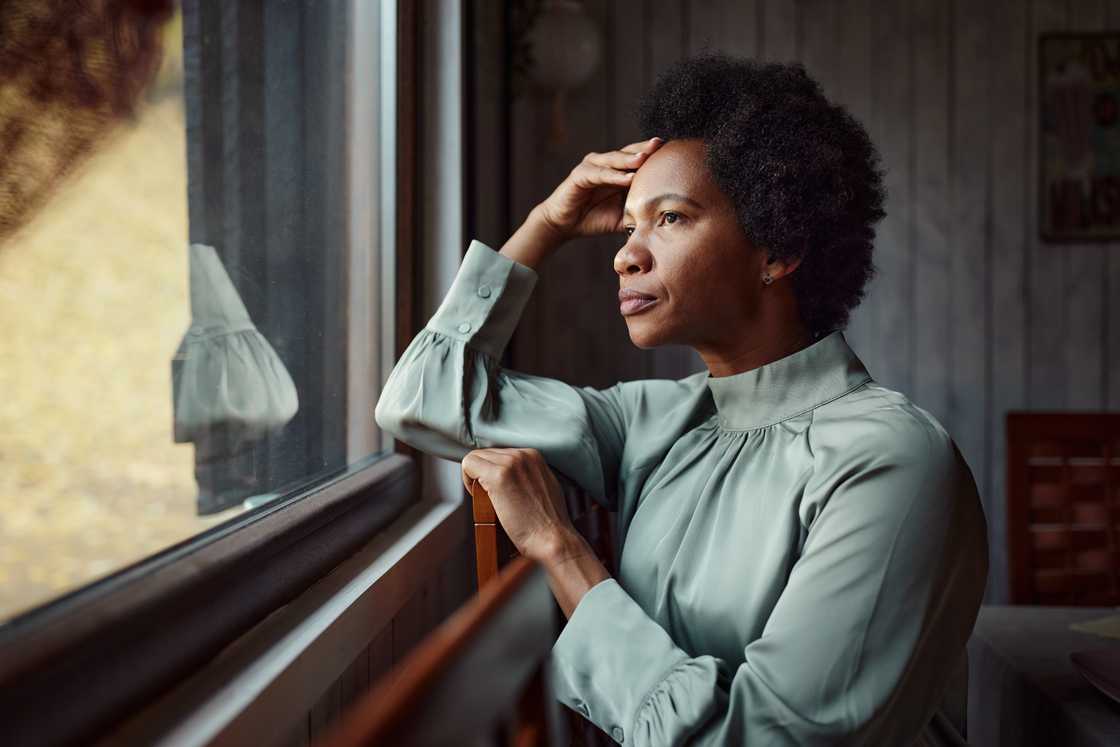 A worried African American woman is looking through the window