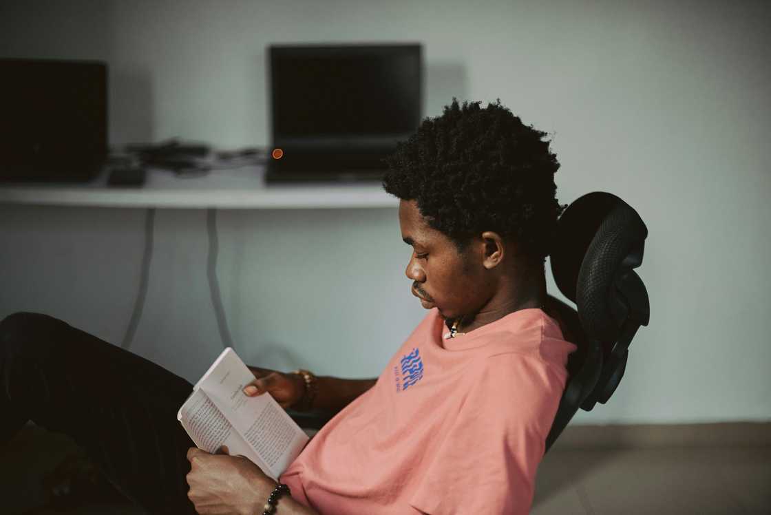 A young man in a pink shirt is reading a book