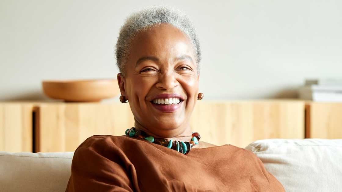 A senior woman in a short afro poses sitting.