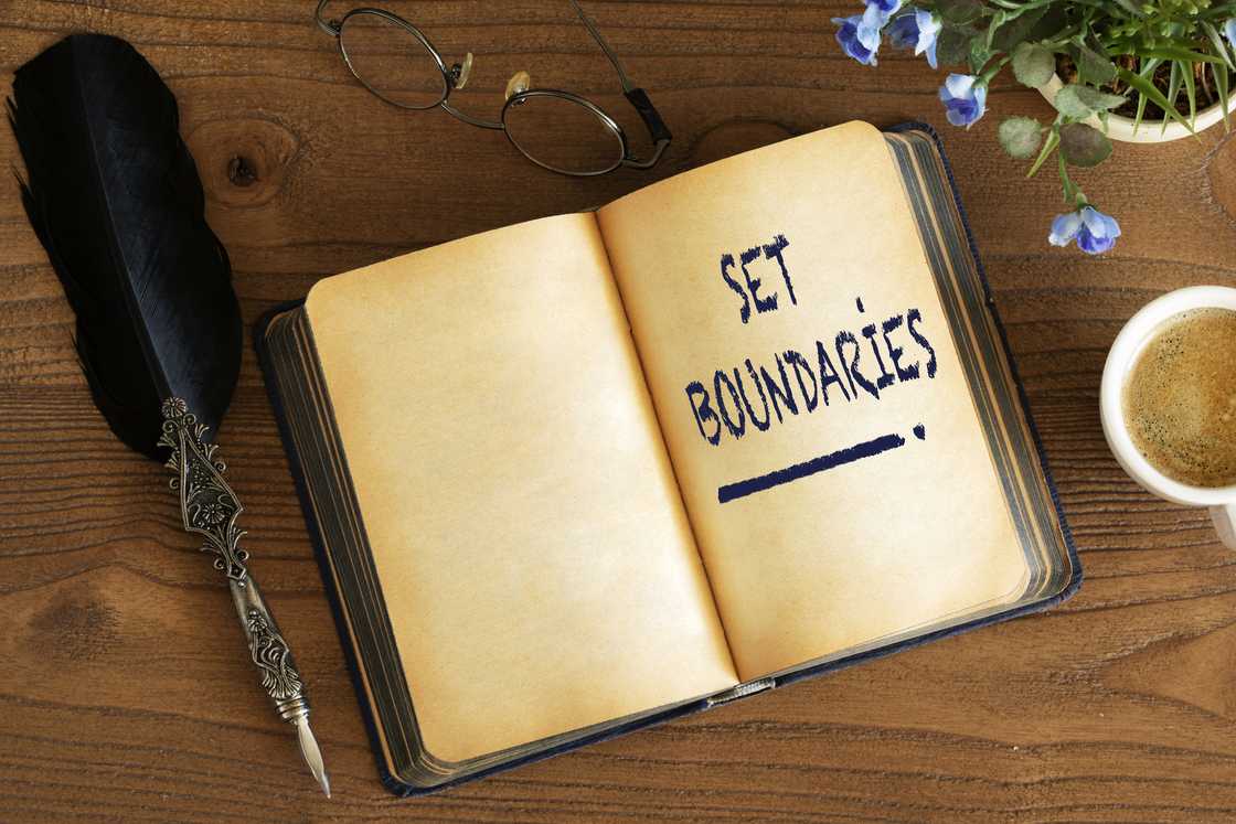 An open journal titled "Boundaries" lies on a desk beside a feather pen. An open journal titled "Boundaries" lies on a desk beside a feather pen.