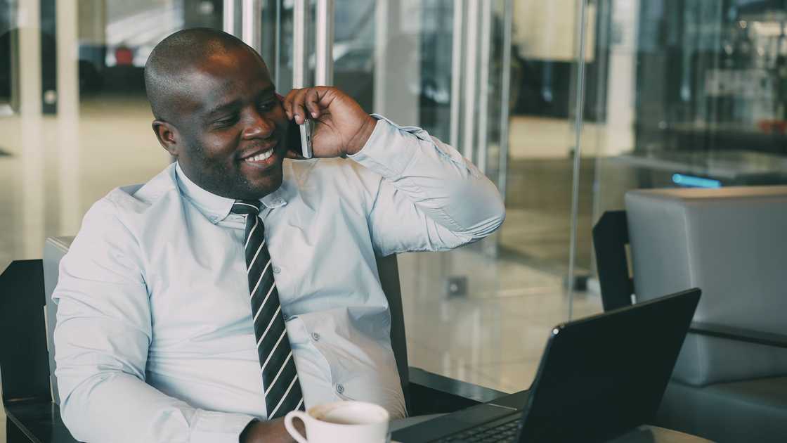 A black man is smiling as he talks on a phone call